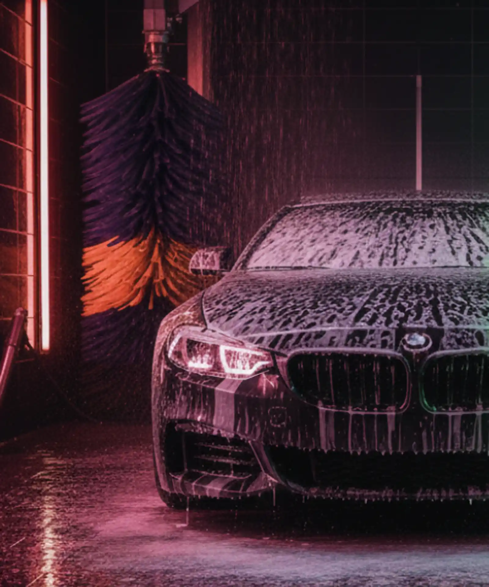 Rear view of a sedan in an automatic car wash bay being sprayed with water and foam, representing operational risks and business insurance for car wash owners.