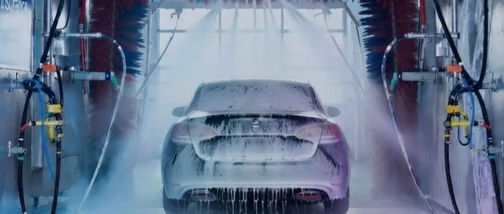 Close-up of the front of a luxury car in an automatic wash bay with vibrant pink and orange lighting, highlighting machinery breakdown and equipment protection for car washes.
