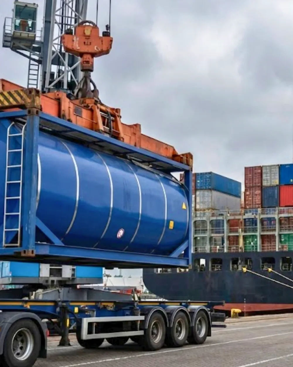 Port crane loading ISO tank container onto semi-trailer at shipping terminal