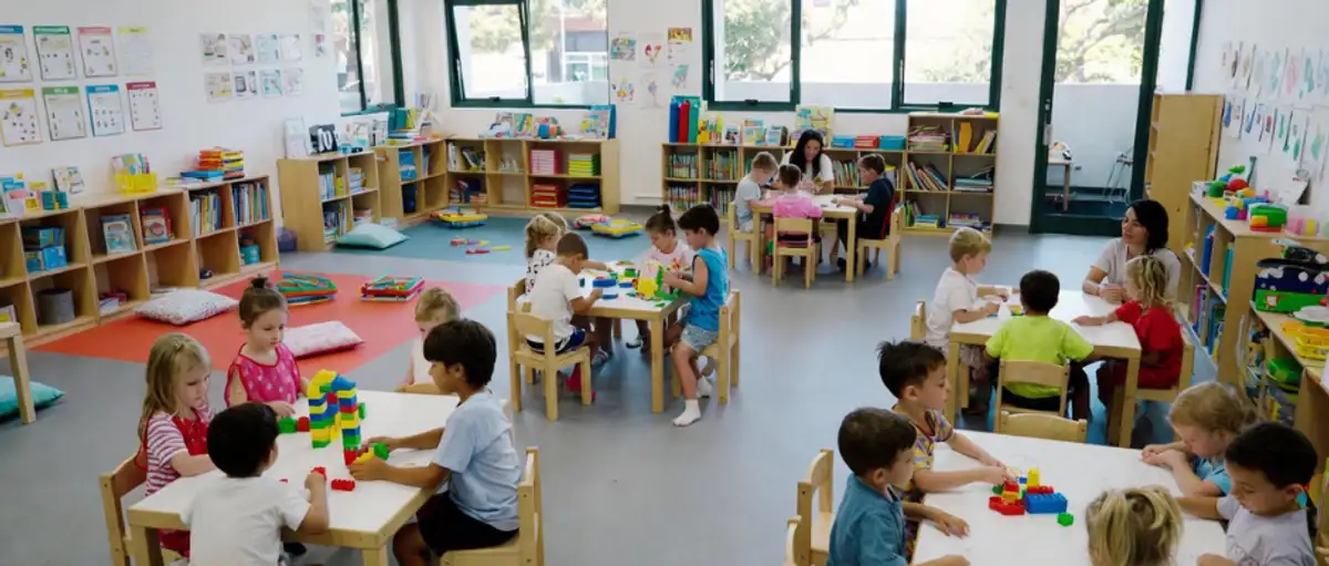 Indoor classroom setting of a commercial daycare centre with young children engaged in educational block play and group activities at small tables.