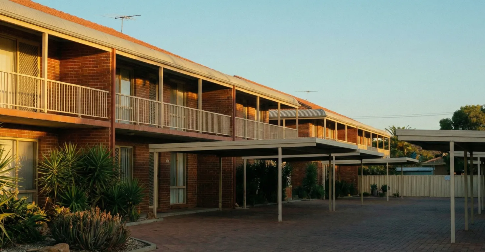 Sunlit multi-dwelling brick townhouse development showcasing shared parking areas covered by non-strata insurance.