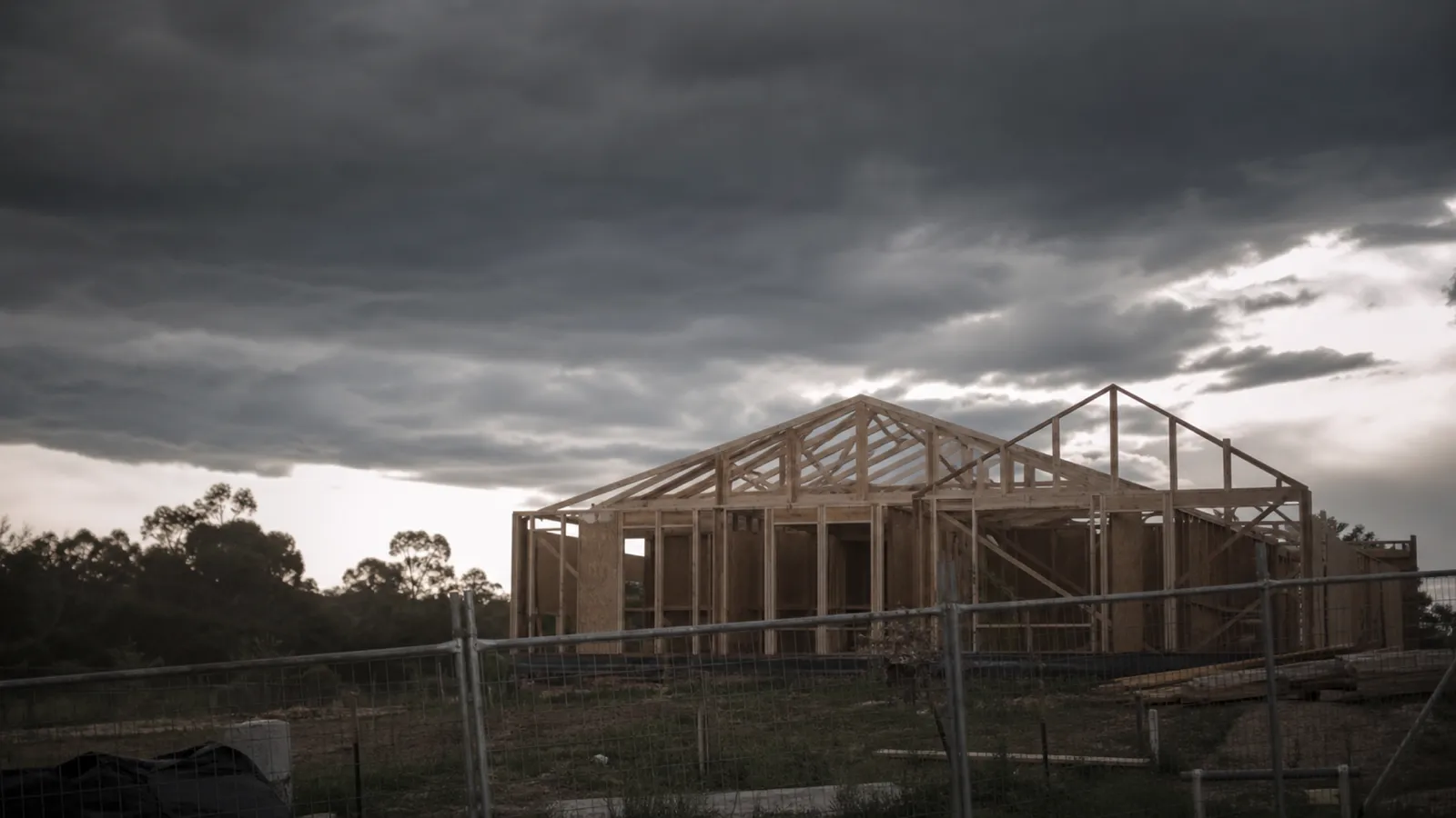 Timber-framed house under construction beneath storm clouds, annual contract works insurance