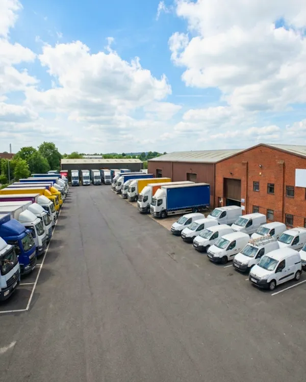 A large fleet of commercial trucks and delivery vans parked at an industrial warehouse facility, representing comprehensive fleet insurance for Australian businesses.