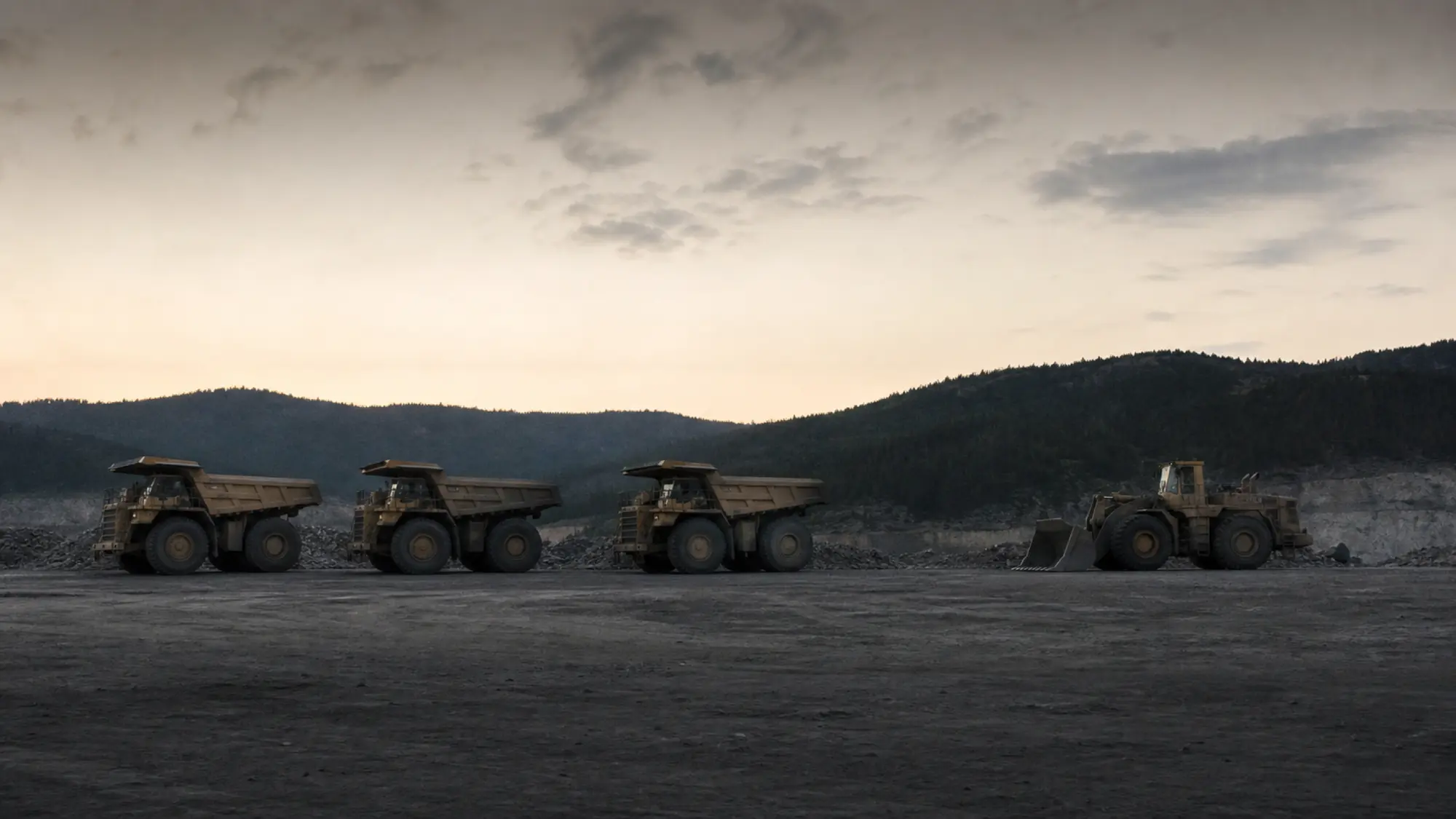Mining haul trucks on a haul road at dusk