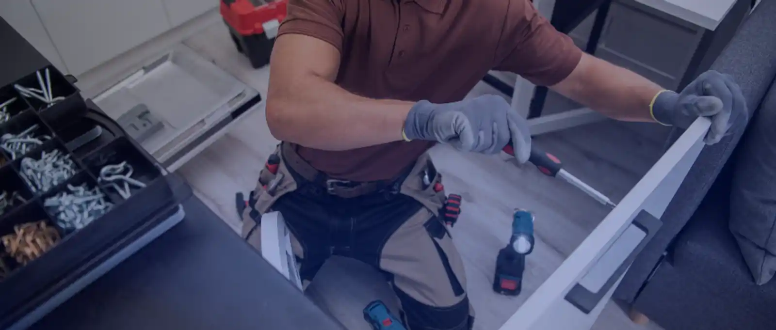 Handyman contractor in work clothes assembling furniture with power drill and tool belt on a residential job site