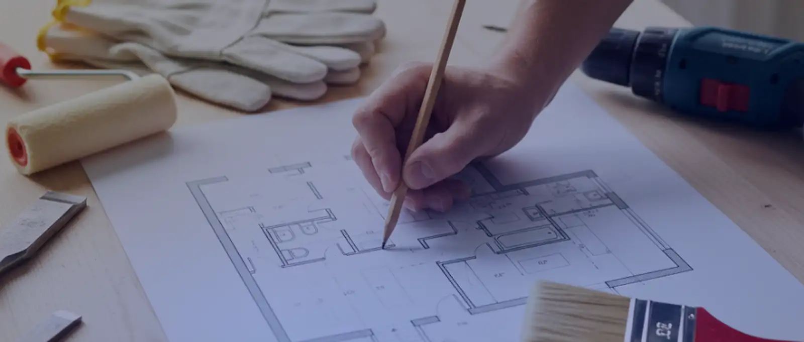 Home renovator drafting architectural floor plan with paint roller, work gloves, and power drill for residential renovation project