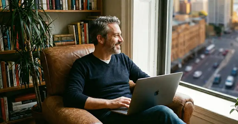 A happy property owner in a home library using a laptop to manage his non-strata insurance policy.