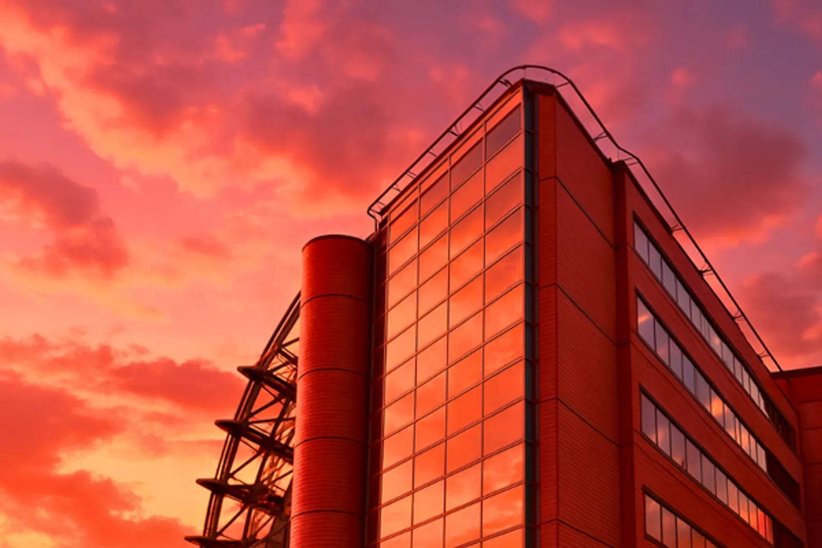 Modern commercial office building with glass facade and cylindrical tower reflecting dramatic sunset sky