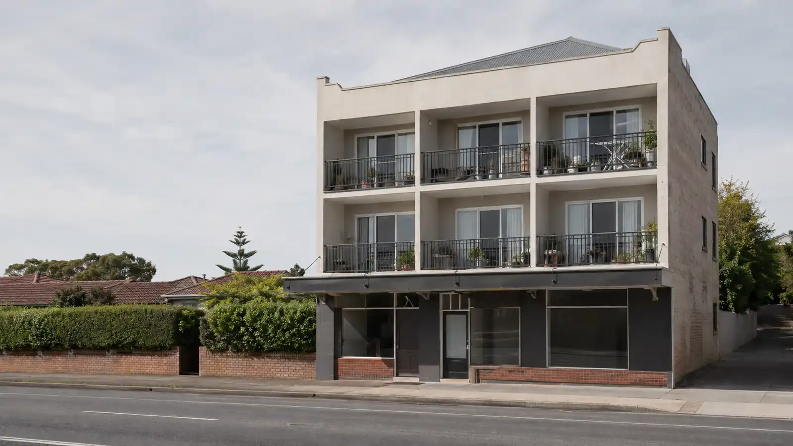 Three-storey rendered mixed-use building with one ground-floor shop and six apartment balconies above