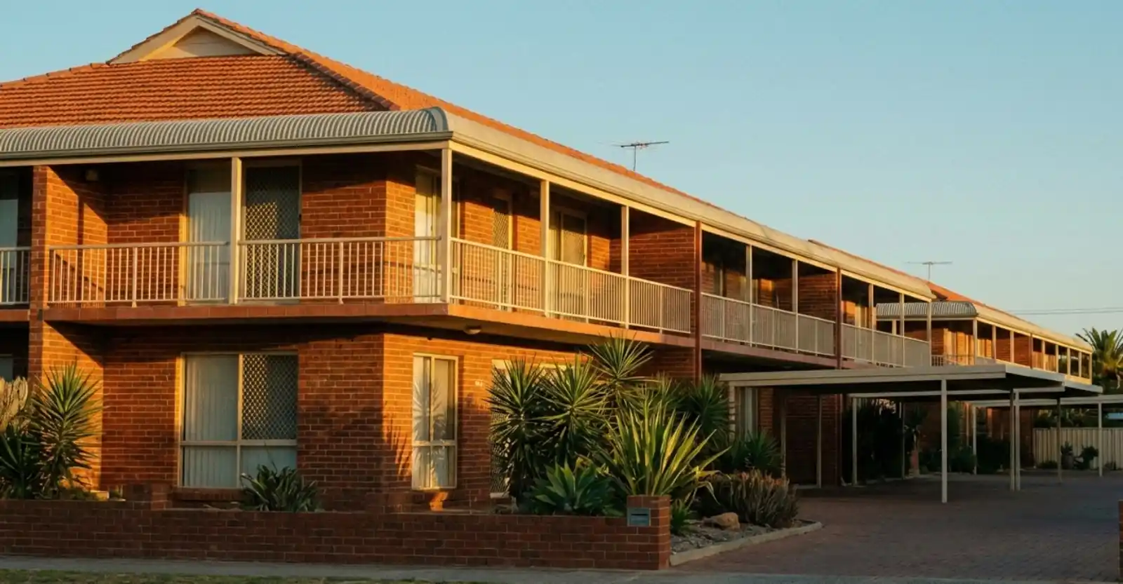 Exterior view of a multi-unit brick residential complex with carports and balconies, illustrating non-strata building insurance coverage.