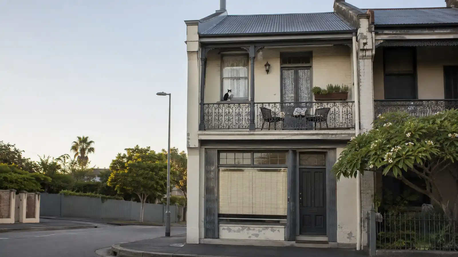 Federation terrace with a small ground-floor shop and a lived-in home above, including balcony chairs and a cat on the sill