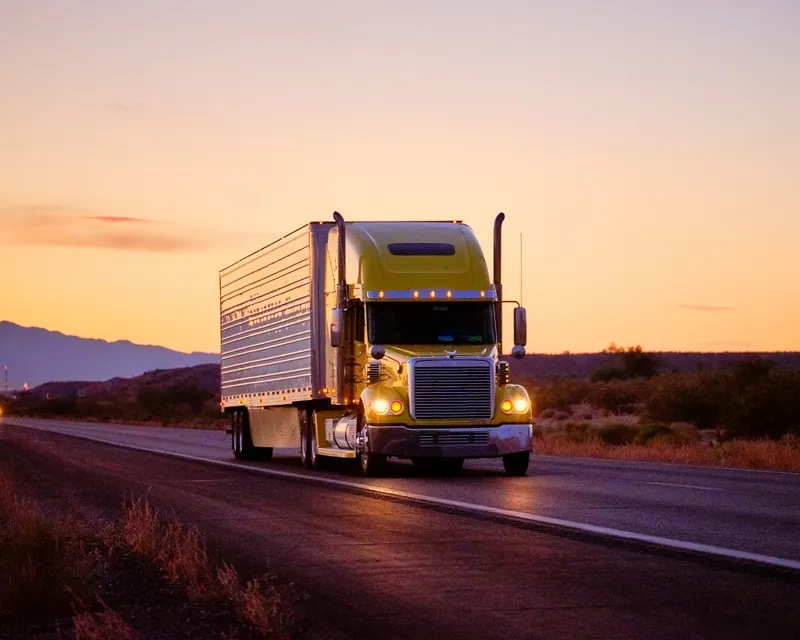 Long-haul yellow freight truck driving on an open highway at sunset, highlighting 24/7 transport coverage and interstate transit insurance.
